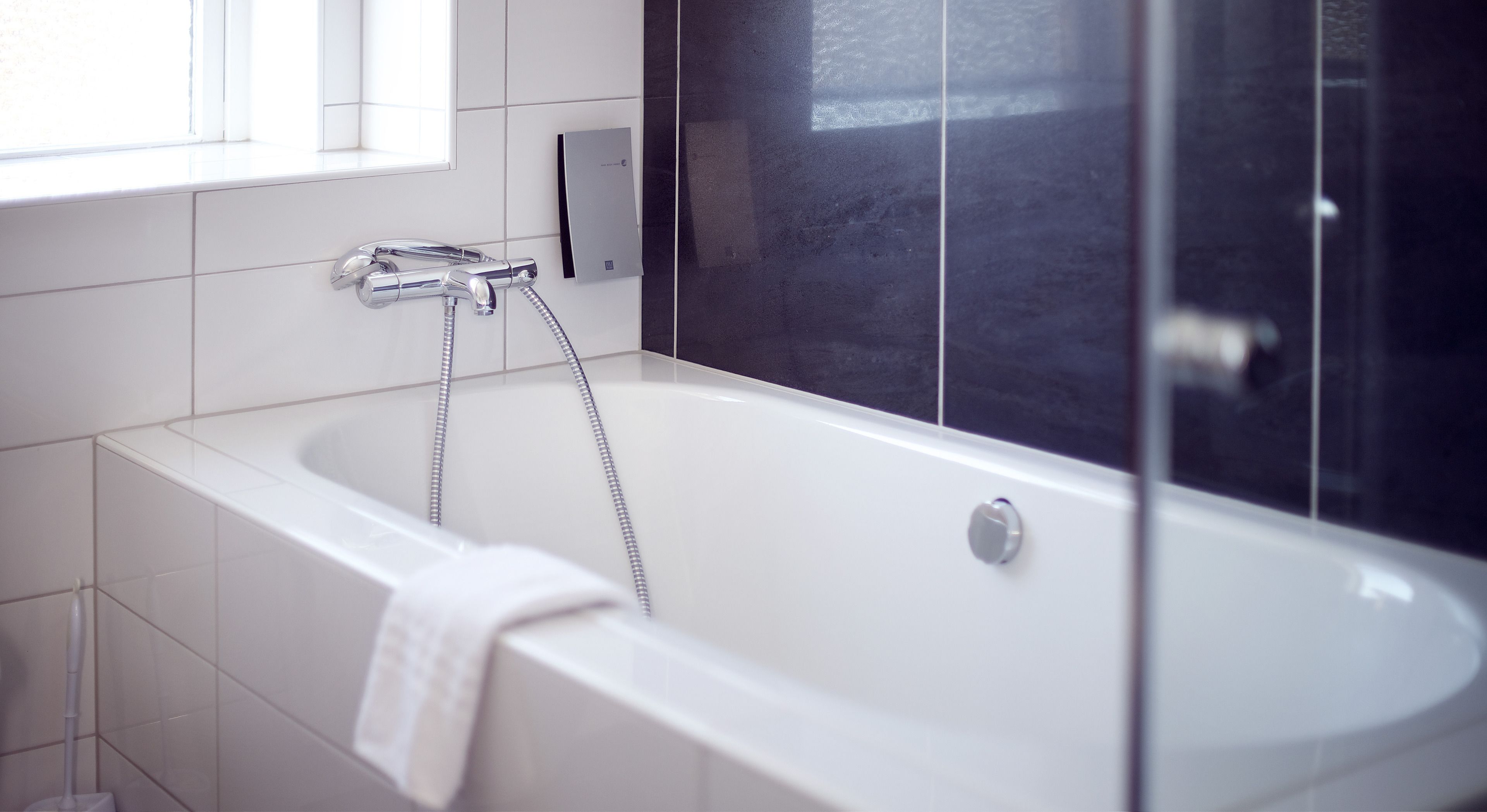Une salle de bain moderne avec une baignoire blanche, une pomme de douche et une serviette accrochée sur le côté.
