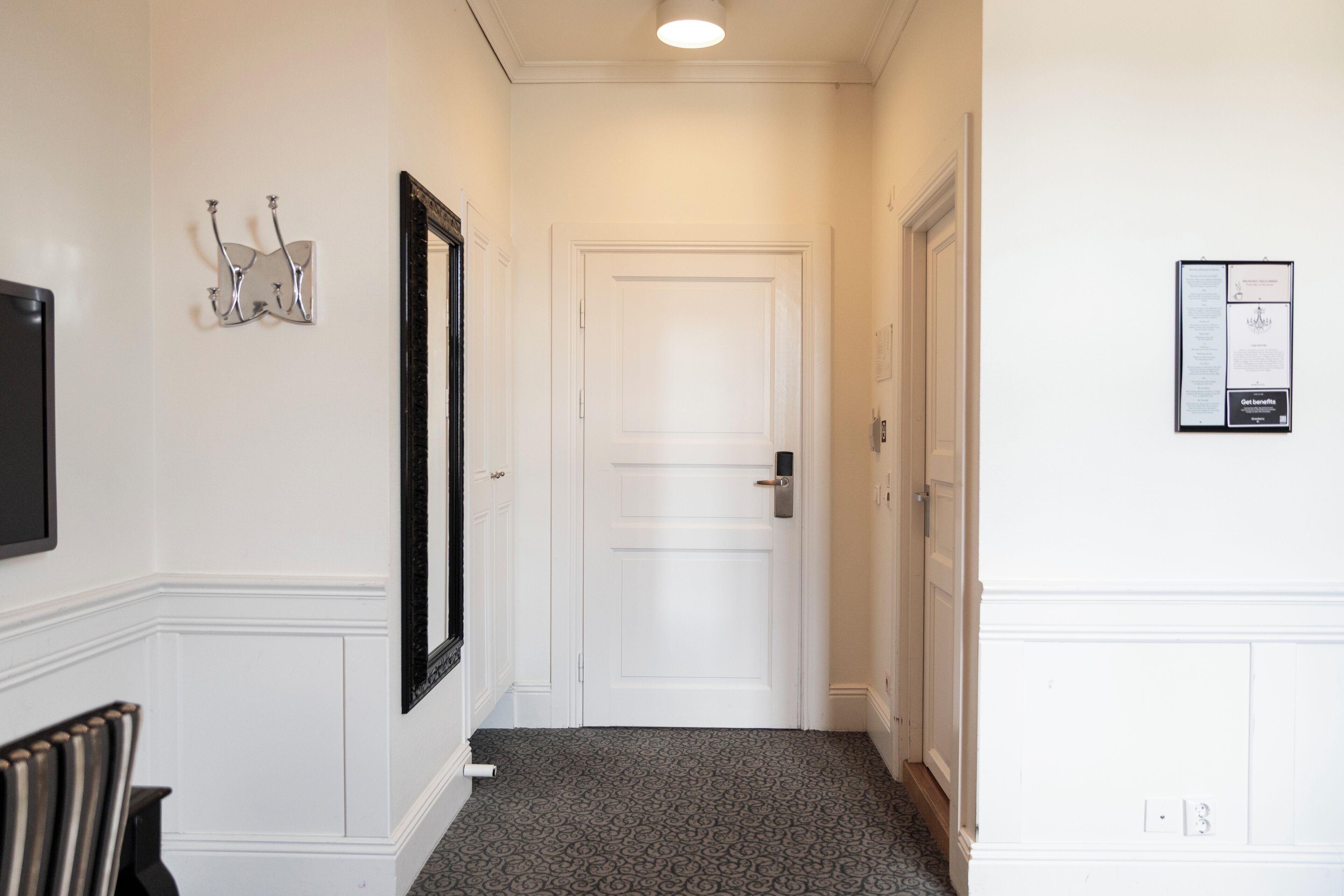 A hallway with a white door, a framed artwork on the wall, and a framed notice.