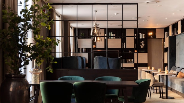 Un comedor moderno con una mesa larga y sillas, una estantería y una zona de estar con sofá y sillones.