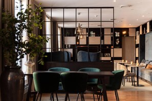 Un espace de salle à manger moderne, avec une longue table et des chaises, une bibliothèque et un coin salon comprenant un canapé et des fauteuils.