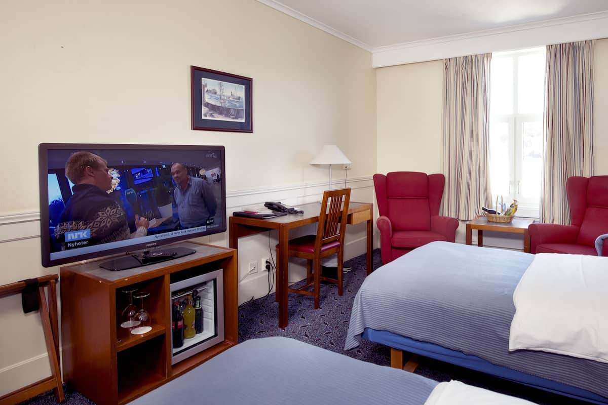 A hotel room with a TV, two red chairs, a desk, and two beds.