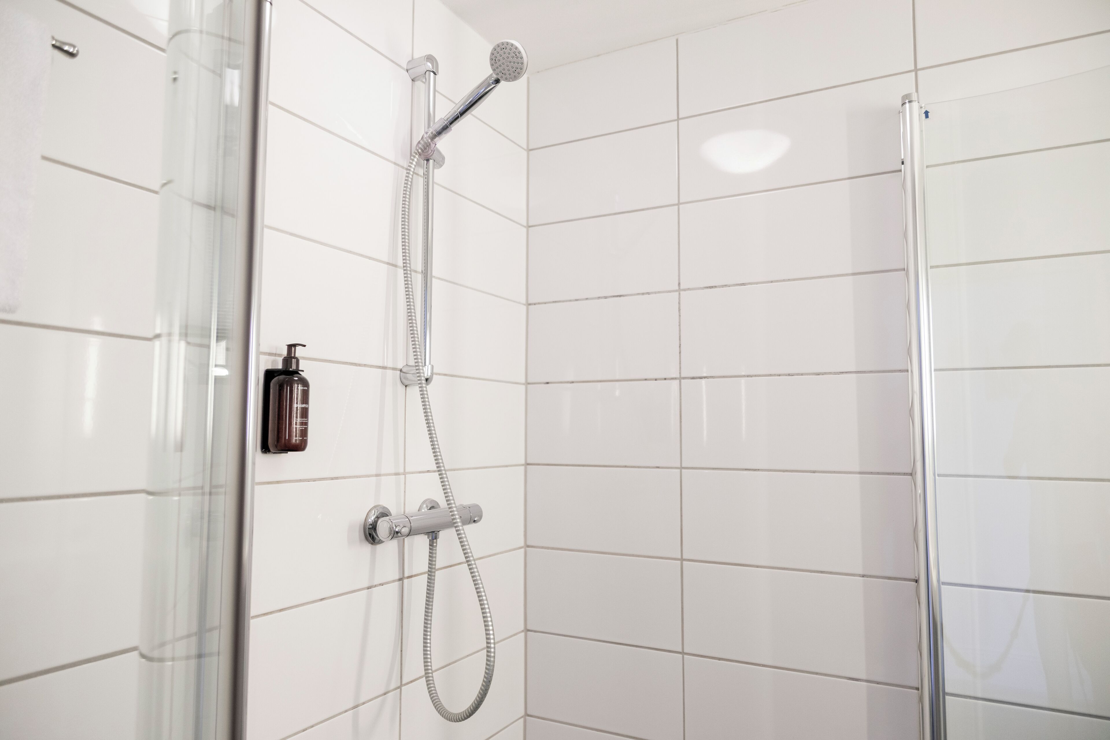 Un baño moderno con paredes de azulejos blancos, cabina de ducha de vidrio y ducha de mano.