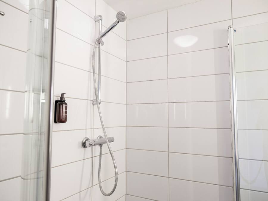 Un baño moderno con paredes de azulejos blancos, cabina de ducha de vidrio y ducha de mano.