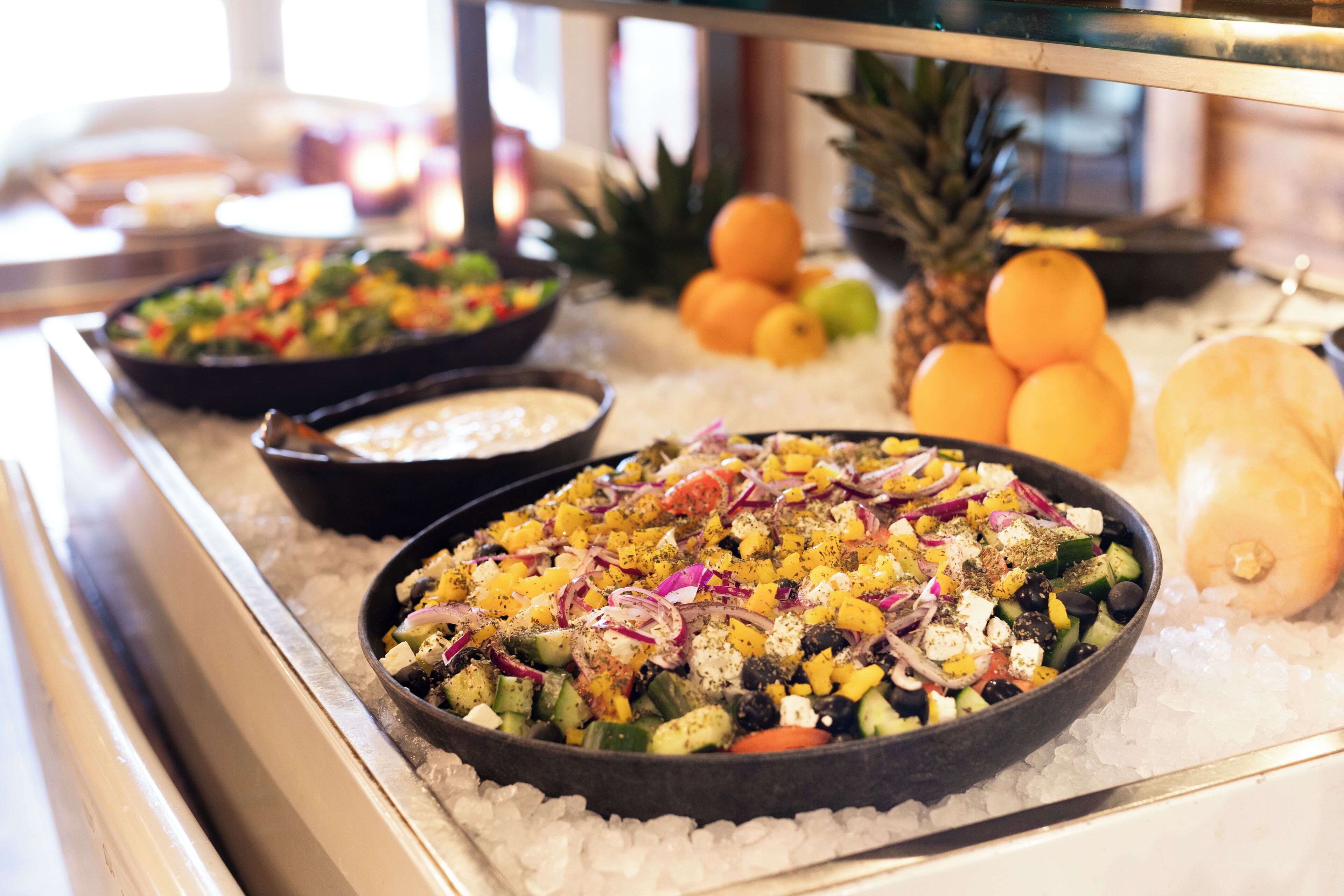 A buffet with various dishes, including a salad with vegetables and feta cheese, and fruits like pineapple and oranges.