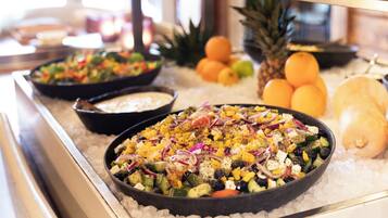 A buffet with various dishes, including a salad with vegetables and feta cheese, and fruits like pineapple and oranges.