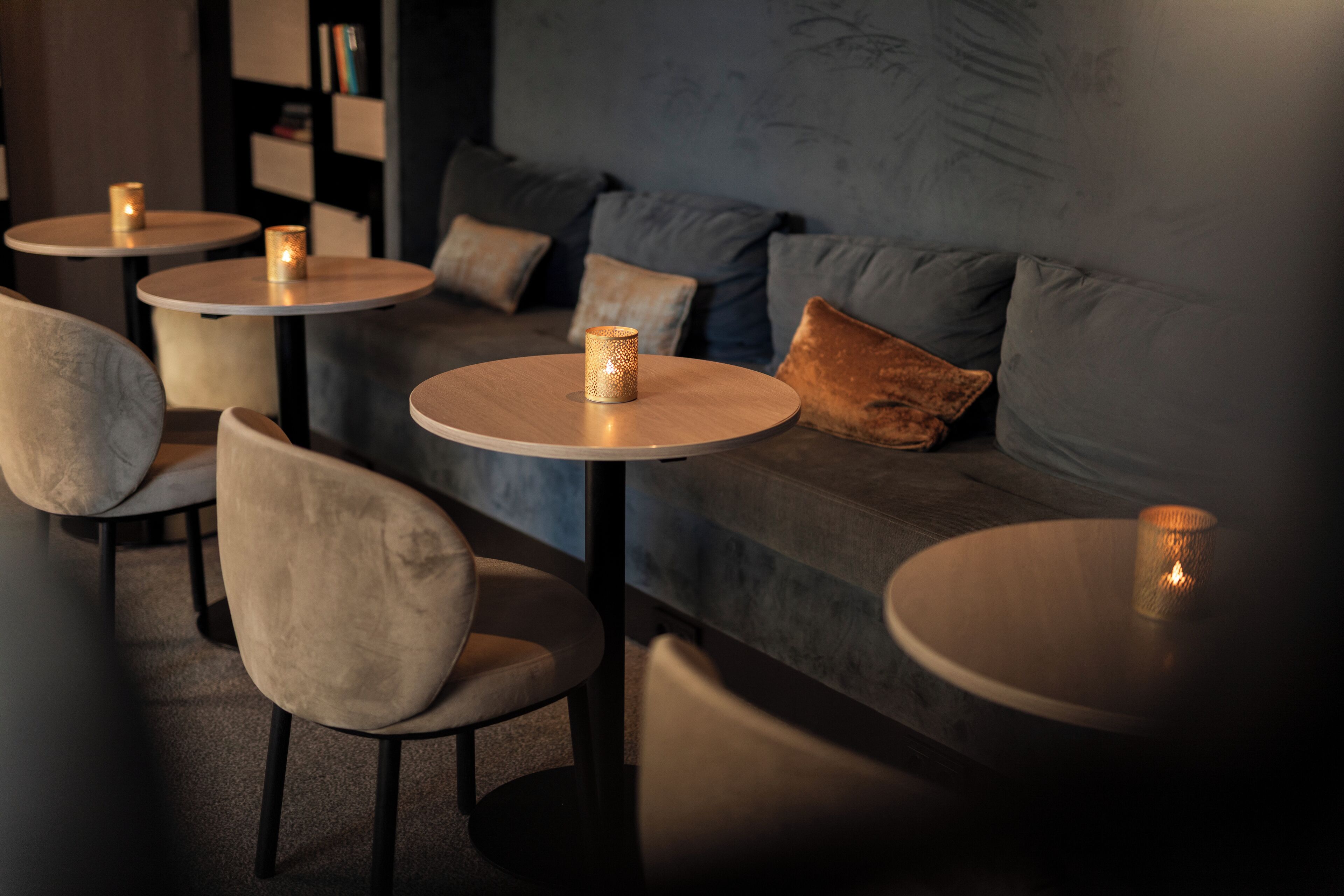 A modern lounge area with round tables and cushioned seating, featuring ambient lighting and a neutral color palette.