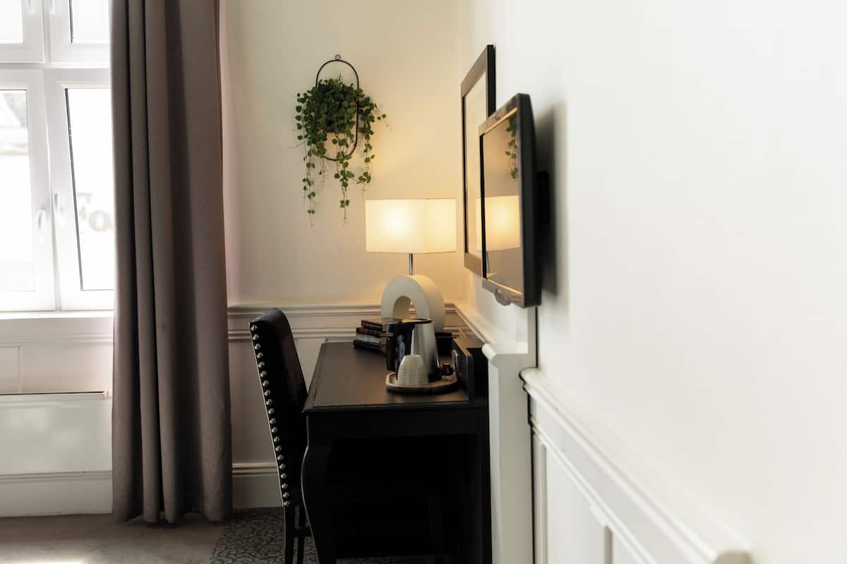 A hotel room with a desk, chair, lamp, and a hanging plant.