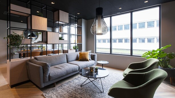 A modern living room with a grey sofa, a round coffee table, and a green armchair. There are shelves with plants and a hanging light fixture. - Scandic Victoria Floro (Floro)