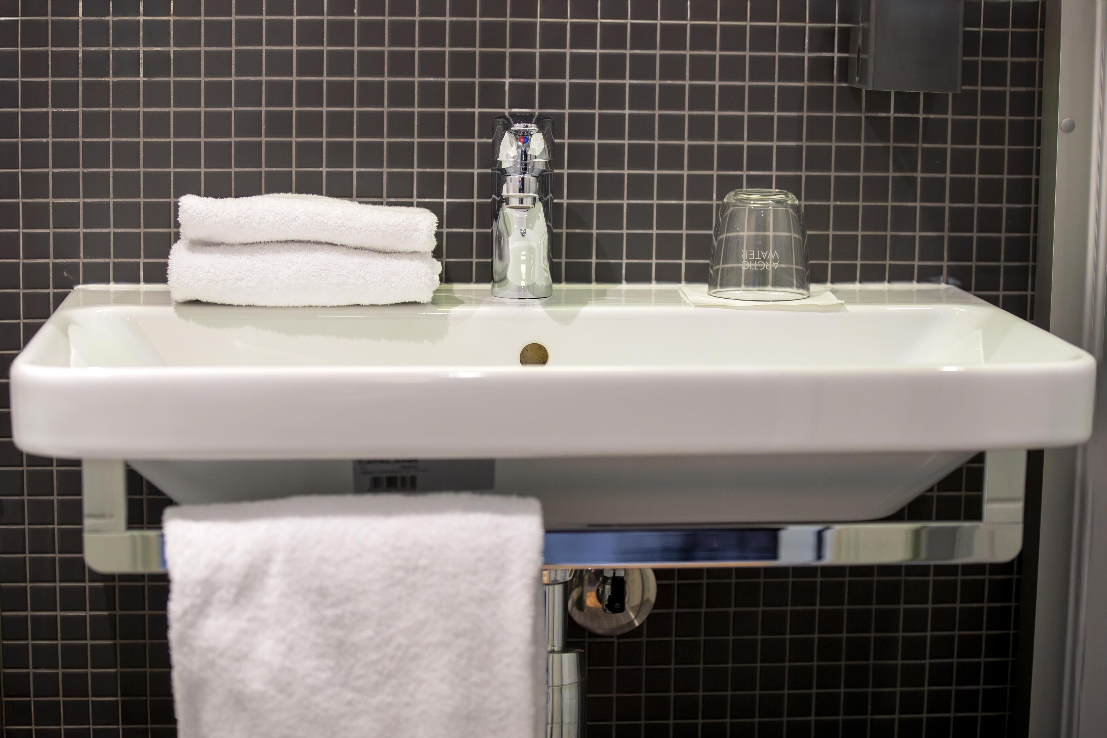 A bathroom sink with a white towel and a glass.