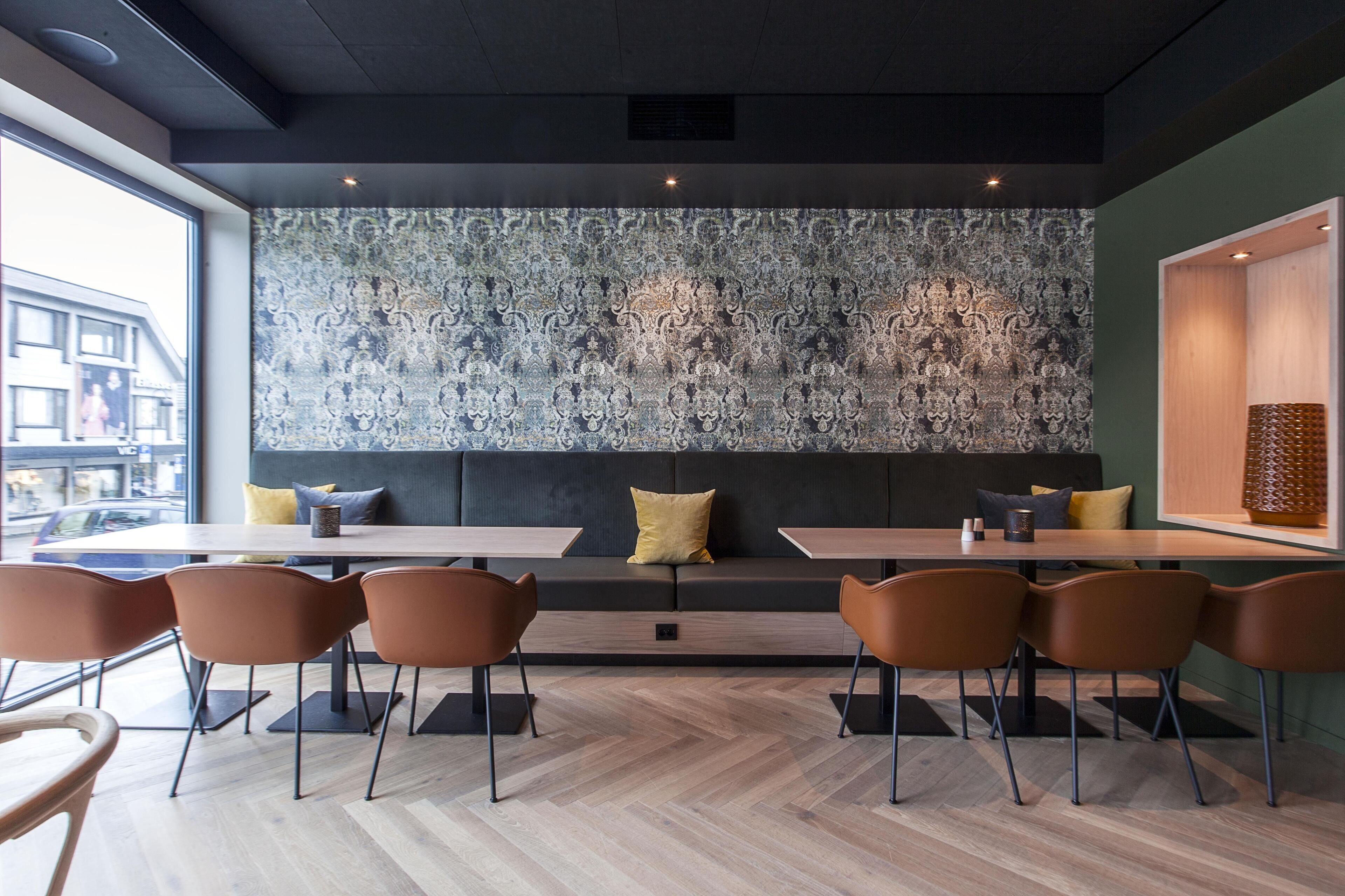 A modern dining area with a patterned wall, a sofa, and several tables and chairs.