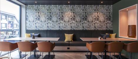A modern dining area with a patterned wall, a sofa, and several tables and chairs.