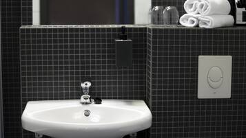 Un baño con un lavamanos blanco, un dispensador de jabón y un perchero con toallas dobladas.