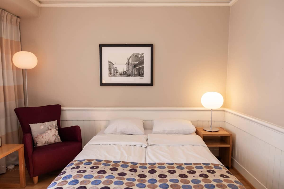 A hotel room with a bed, a chair, a bedside table, a lamp, and a framed picture on the wall.
