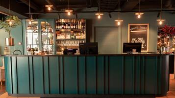 Una zona de bar con mostrador verde azulado, estantes con botellas, un menú en la pizarra y luces colgantes.