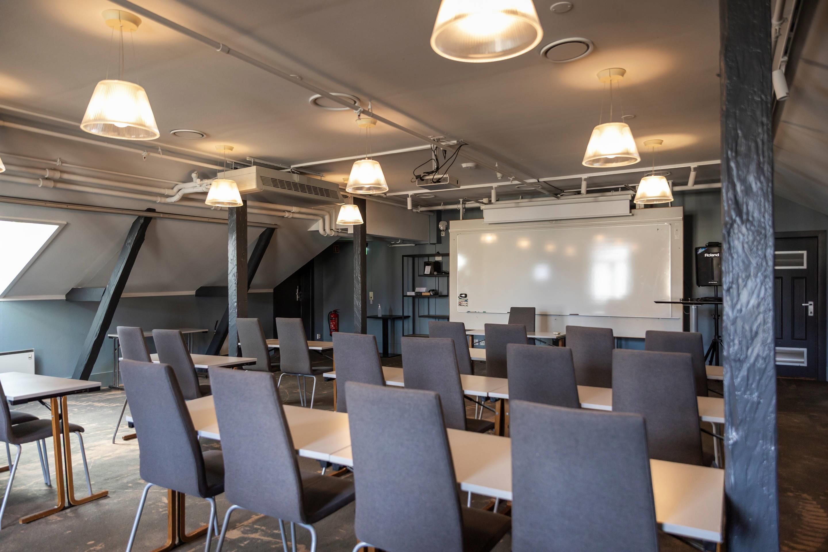A conference room with tables, chairs, a whiteboard, and pendant lighting.