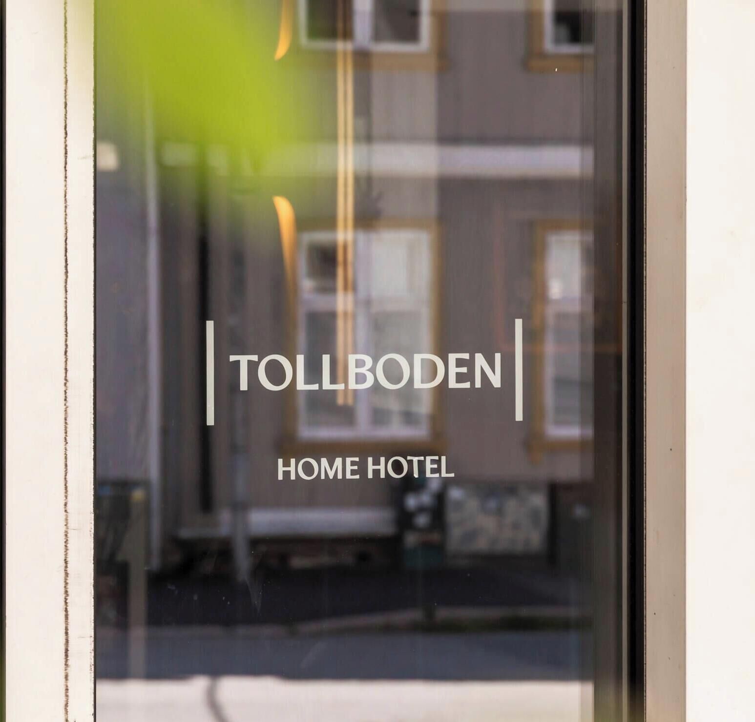 Ein Fenster mit dem Schriftzug 'TOLLBODEN HOME HOTEL' und einem unscharfen Hintergrund eines Gebäudes.