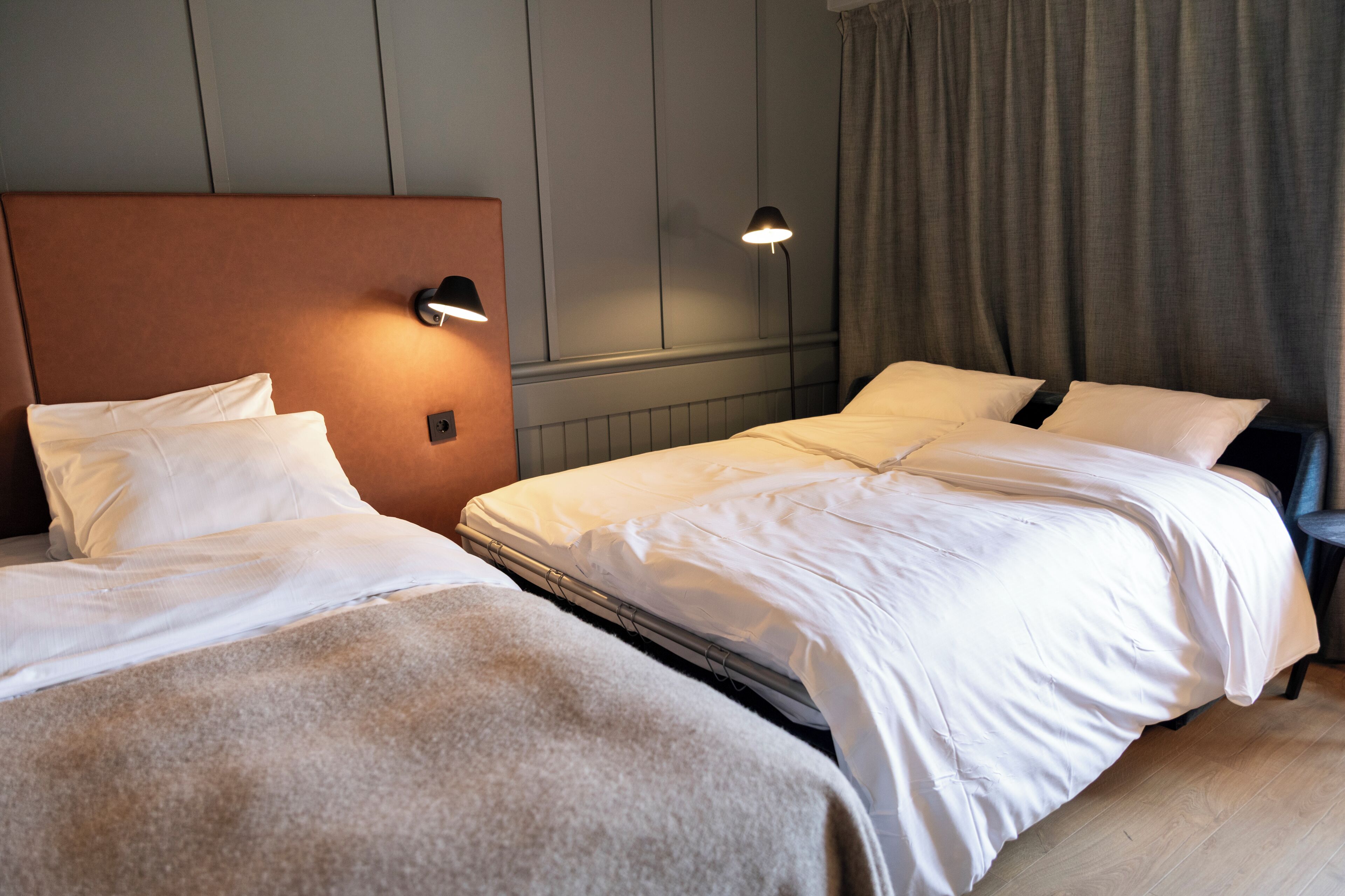 Une chambre d’hôtel avec deux lits, une tête de lit, des lampes de chevet et un rideau.