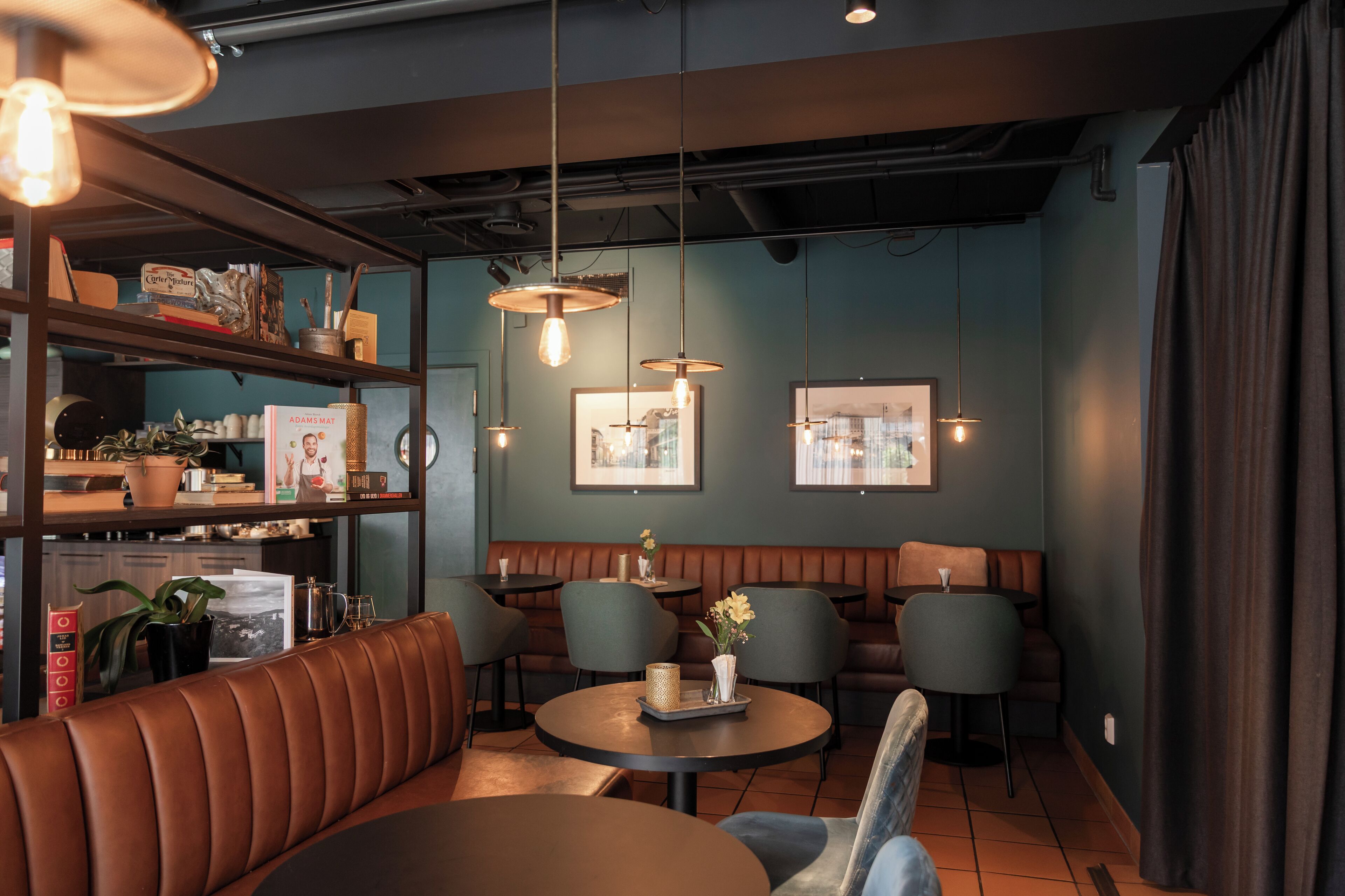 A modern interior with leather seating, tables, pendant lighting, and framed artwork on the walls.