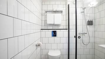 A modern bathroom with white tiles, a glass-enclosed shower, a toilet, and a shelf with toiletries.