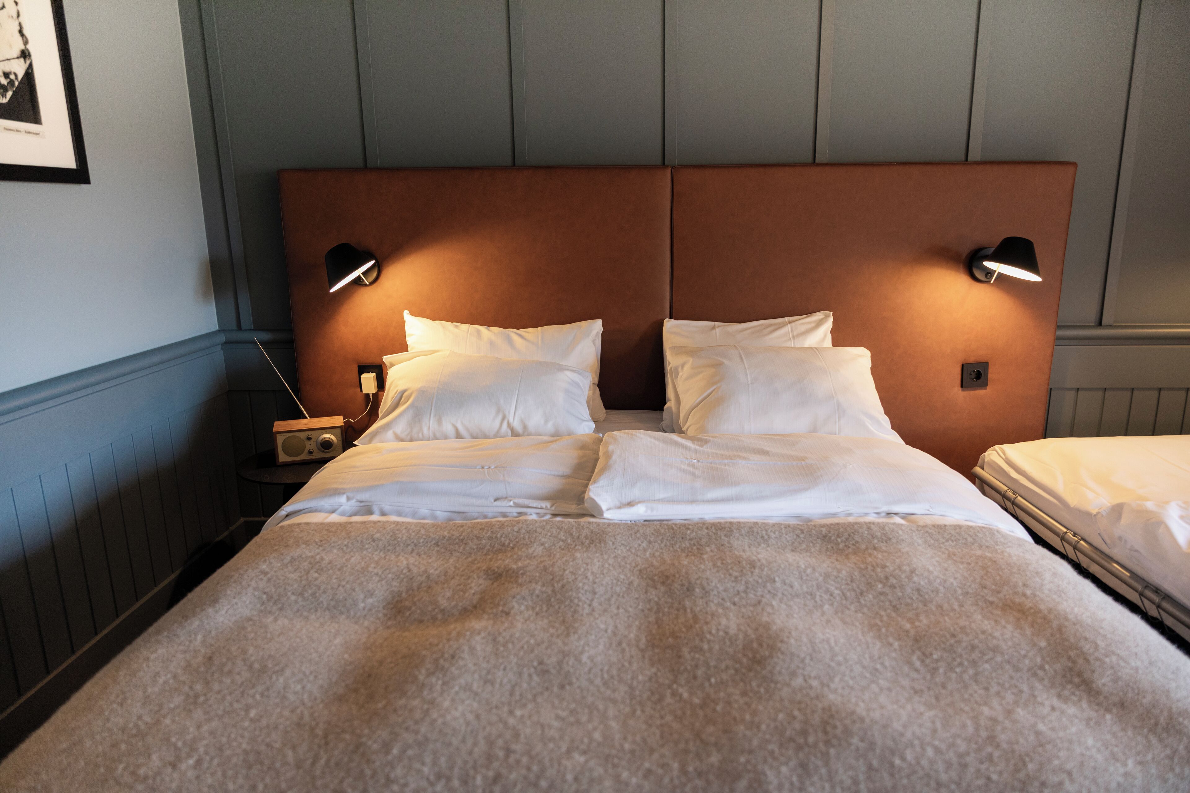 A double bed with a brown headboard, two bedside tables with lamps, and a framed picture on the wall.