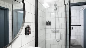Un baño moderno con azulejos blancos, mampara de cristal, inodoro y lavamanos.