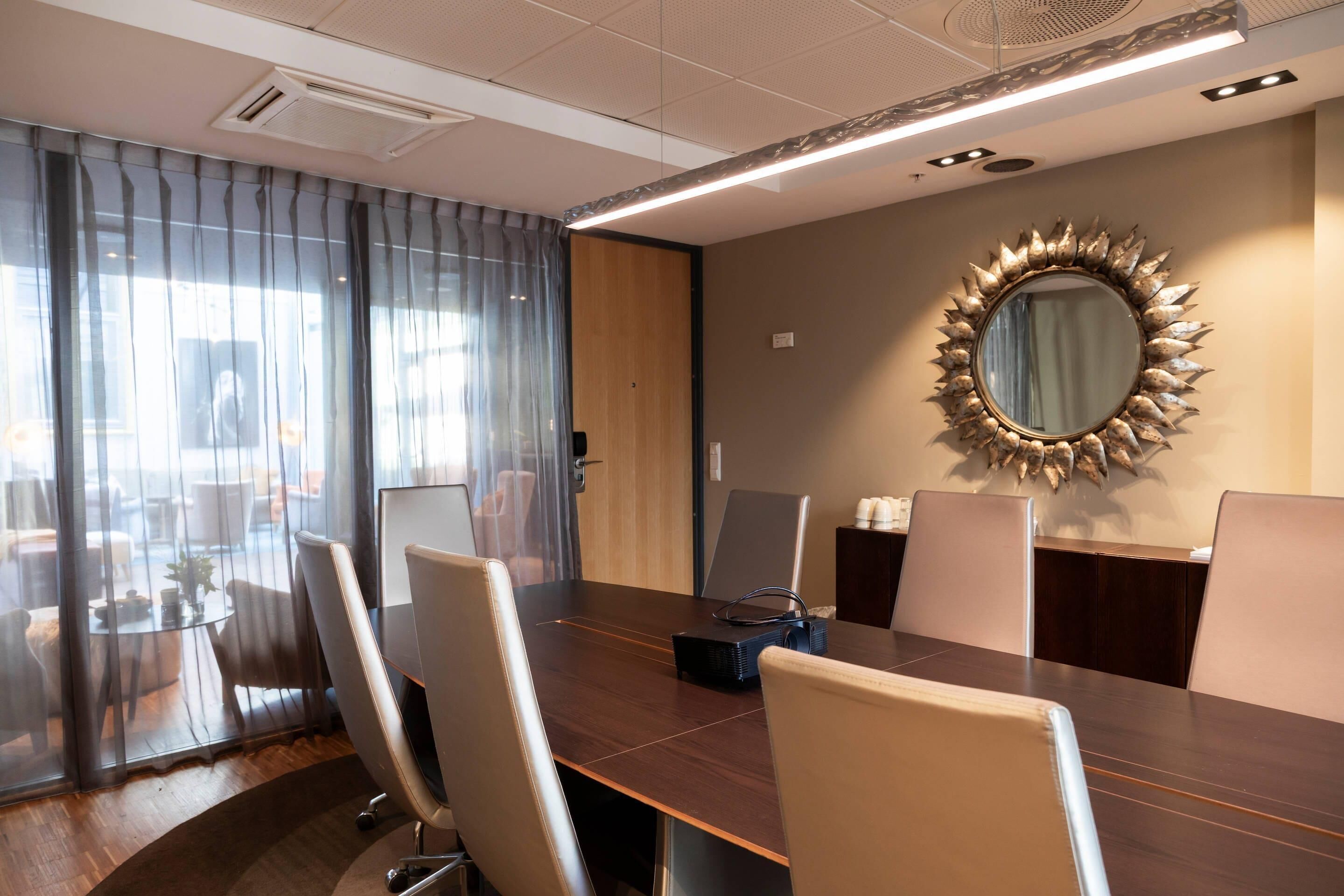 A conference room with a large table, chairs, a projector, and a decorative mirror on the wall.