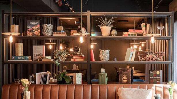 Un interior moderno con un área de asientos tipo banca de cuero, estantes con libros y objetos decorativos, e iluminación colgante.