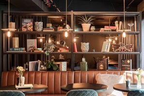 A modern interior with a leather booth seating area, shelves with books and decorative items, and pendant lighting. - Home Hotel Tollboden (Drammen)