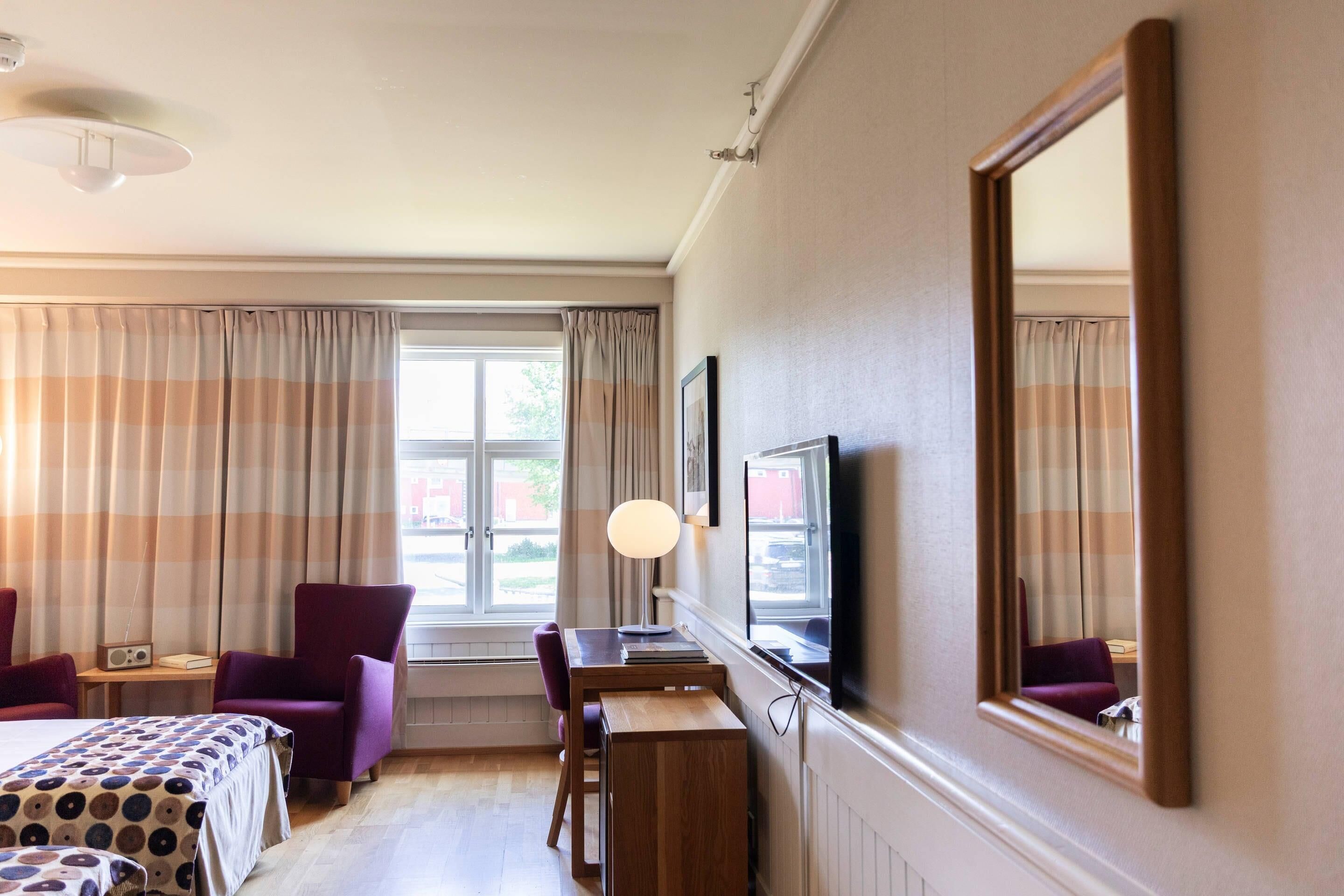 A hotel room with a bed, a desk, a chair, a TV, and a window with curtains.