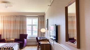 A hotel room with a bed, a desk, a chair, a TV, and a window with curtains.
