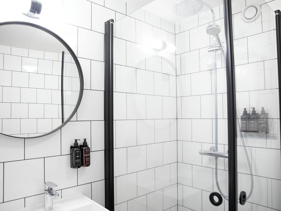 A modern bathroom with white tiles, a round mirror, a glass-enclosed shower, and a sink with a faucet.