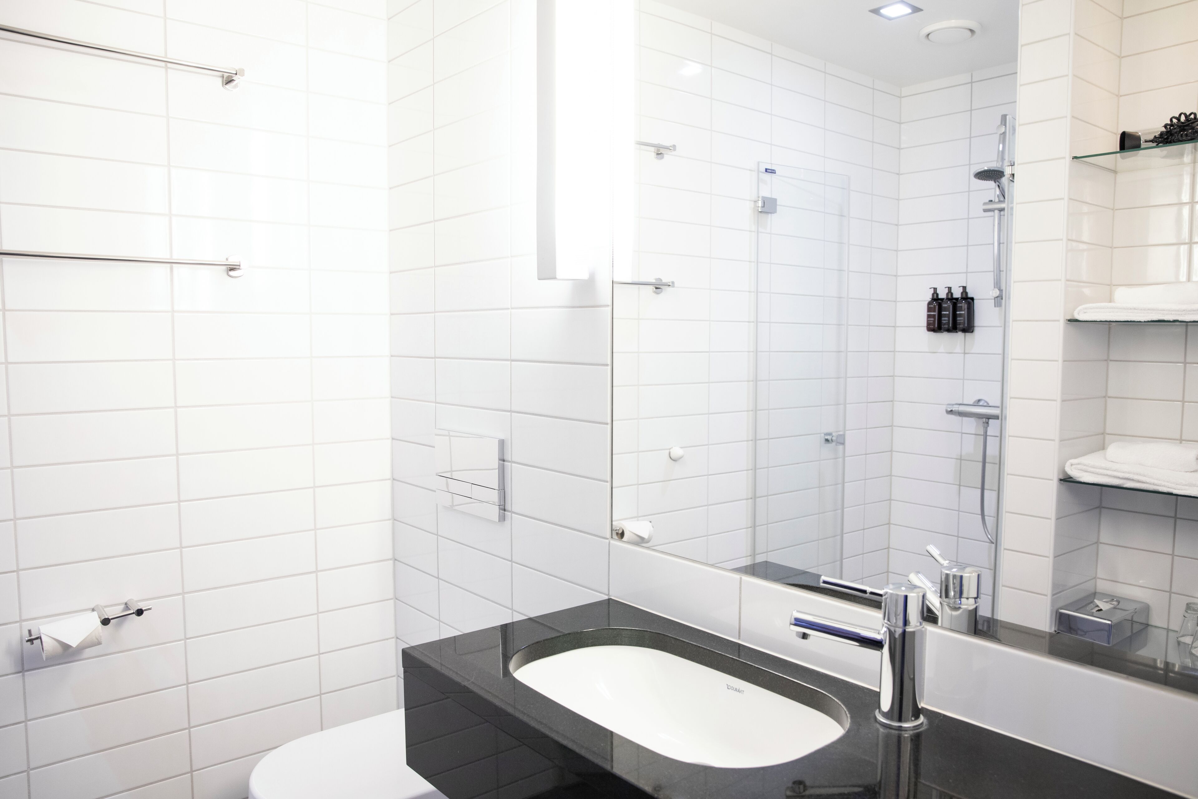 Un baño moderno con azulejos blancos, un lavamanos negro y una cabina de ducha de vidrio.