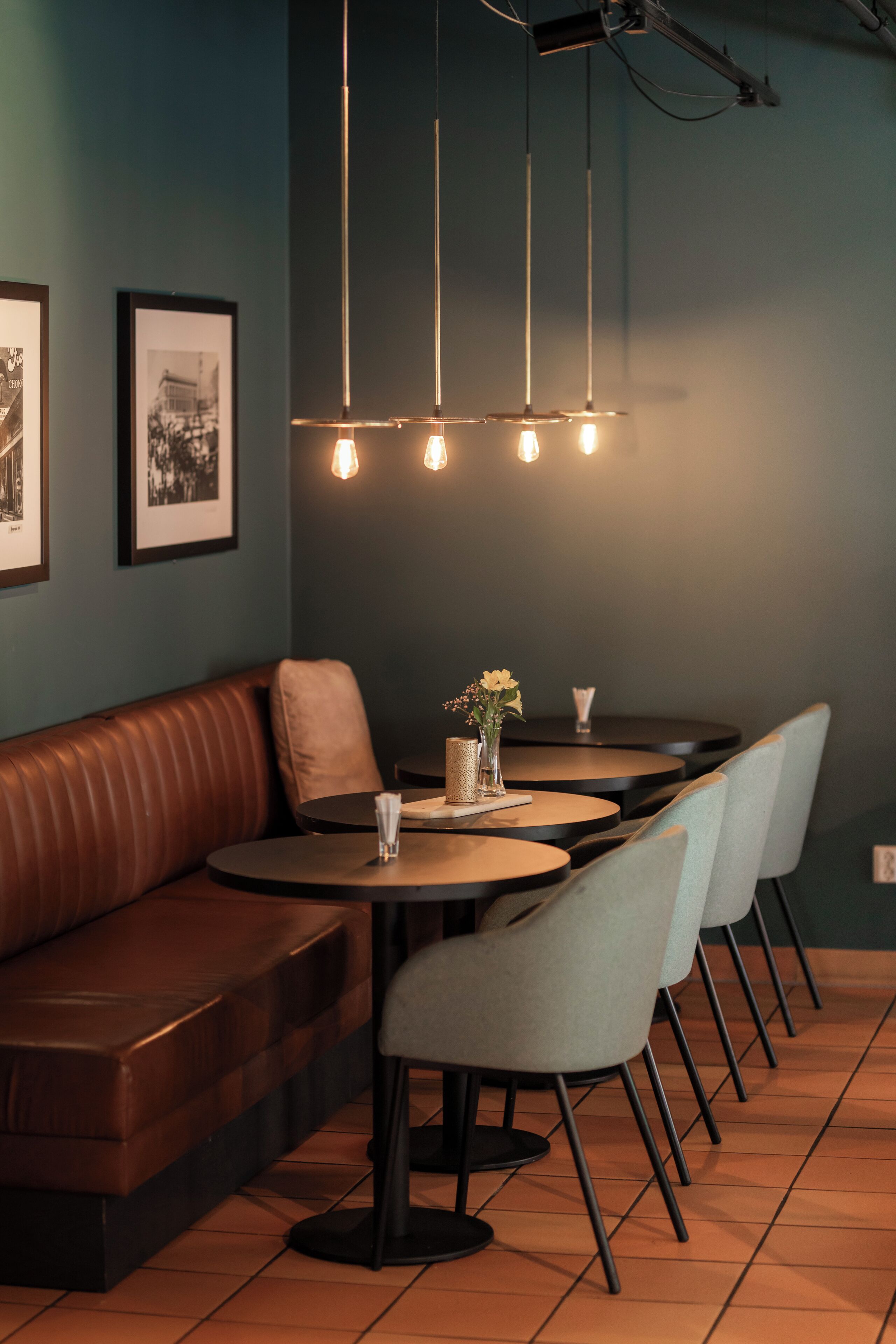Een restaurantinterieur met een bruine leren zithoek, ronde tafels en lichtgrijze stoelen.
