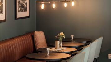 Een restaurantinterieur met een bruine leren zithoek, ronde tafels en lichtgrijze stoelen.
