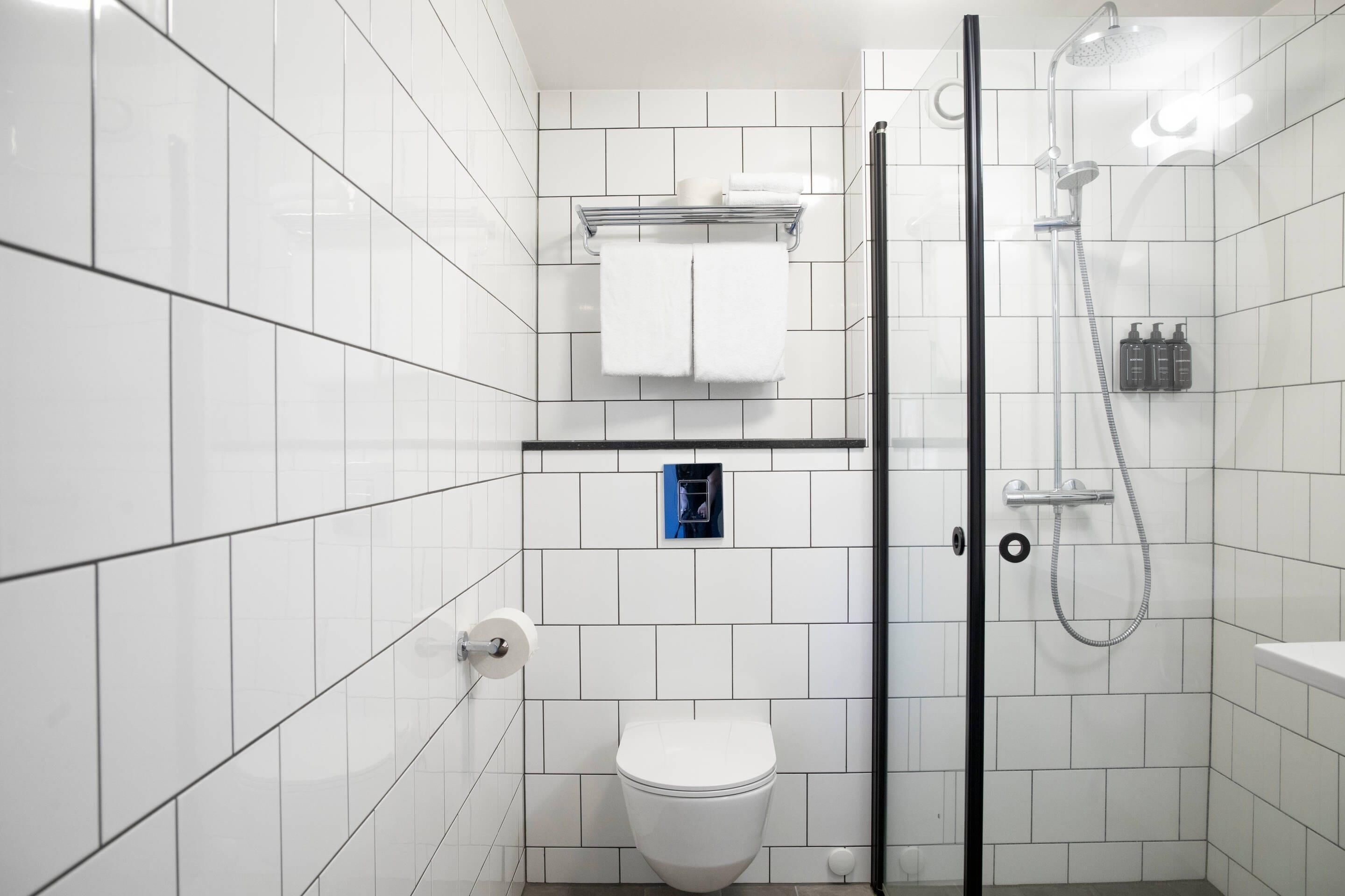 Un baño moderno con azulejos blancos, un inodoro, una ducha y un perchero para toallas.
