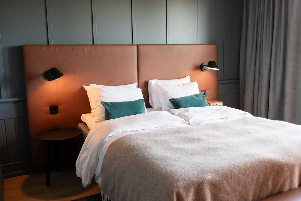 A hotel room with a large bed, two bedside tables, and a headboard with integrated lighting.