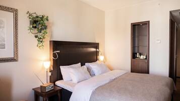 A hotel room with a bed, bedside lamps, a small table, a plant, a framed picture, and a wardrobe.