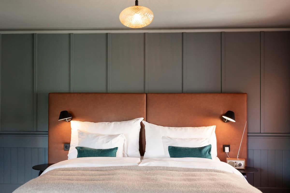 A neatly made bed with pillows, a bedside lamp, and a radio on a bedside table.