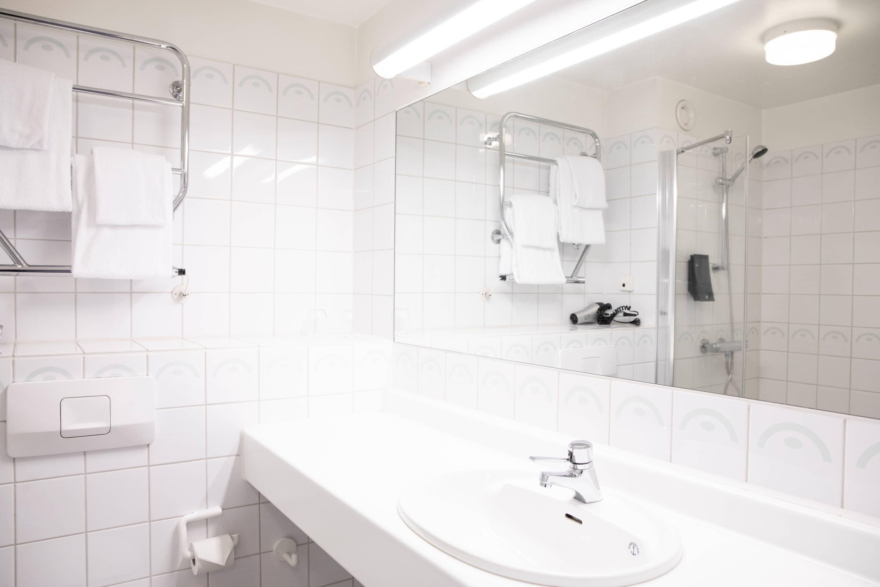 A modern bathroom with a white sink, a mirror, a towel rack, and a shower area.