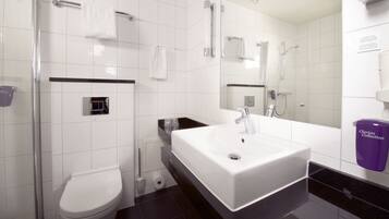 Une salle de bain moderne avec des toilettes blanches, un grand lavabo blanc, un espace douche et un miroir.