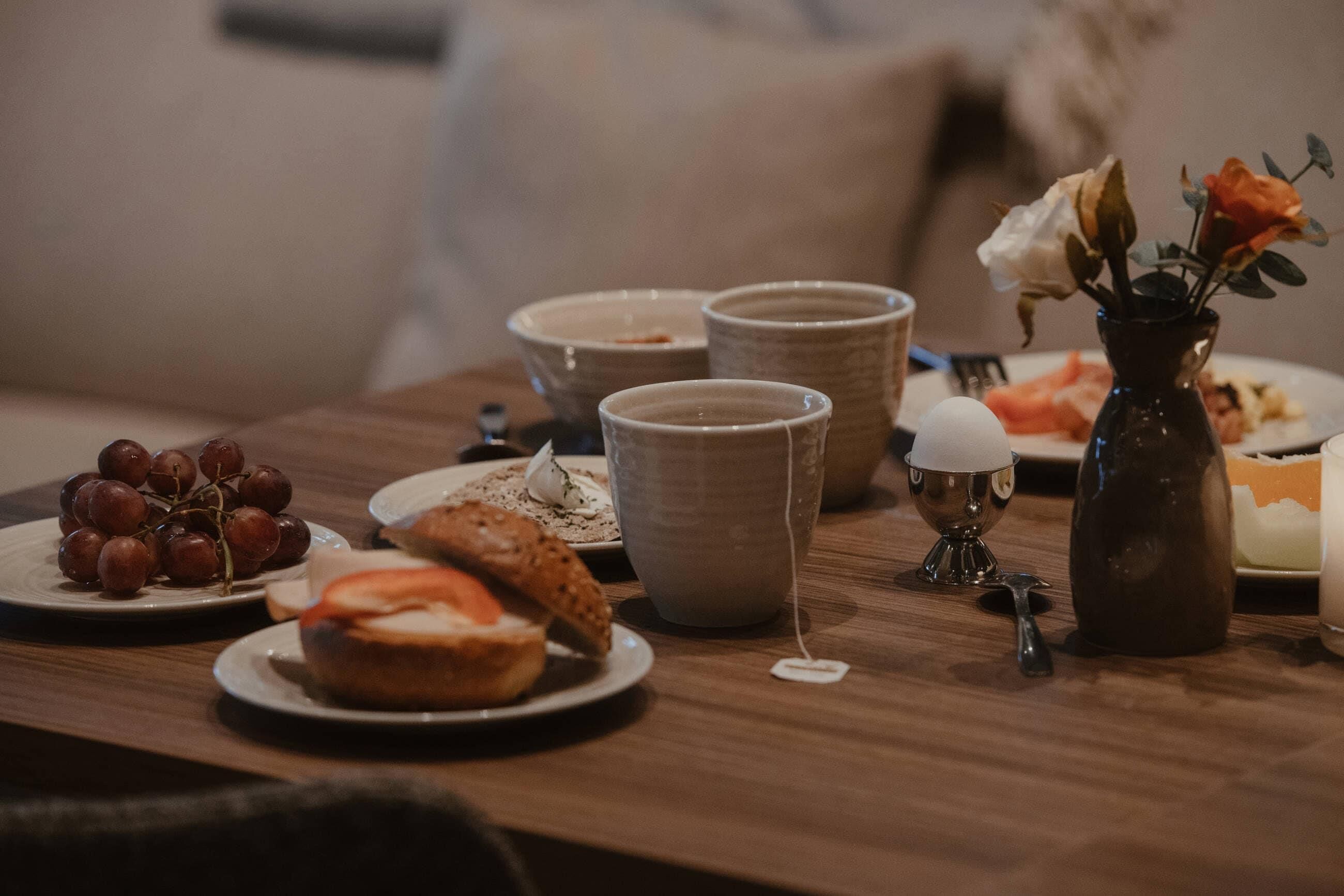 Una mesa de comedor con platos de comida, un jarrón con flores y una cafetera.