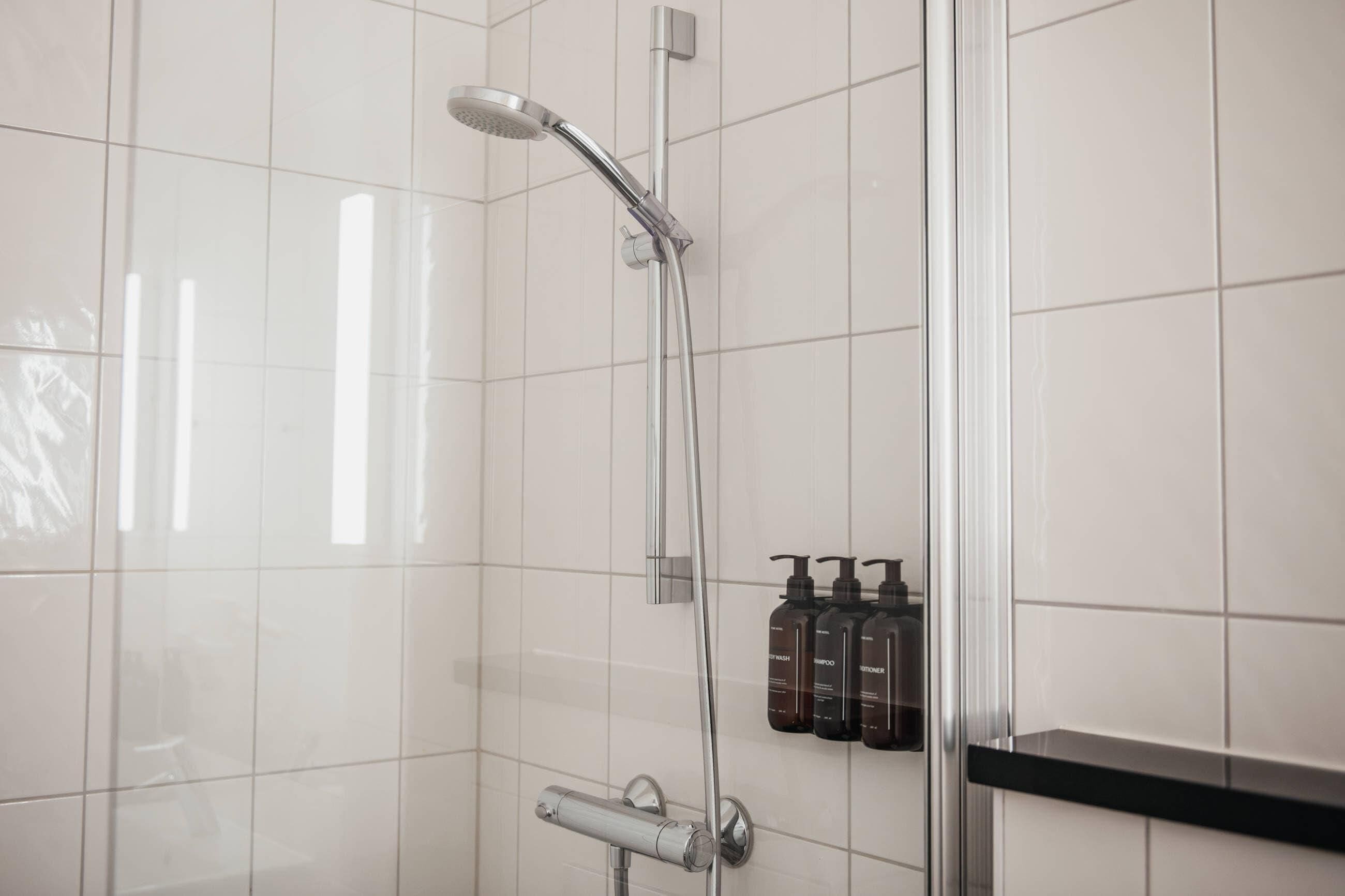 Ducha con cabezal de ducha manual, grifo empotrado en la pared y repisa con botellas de champú.