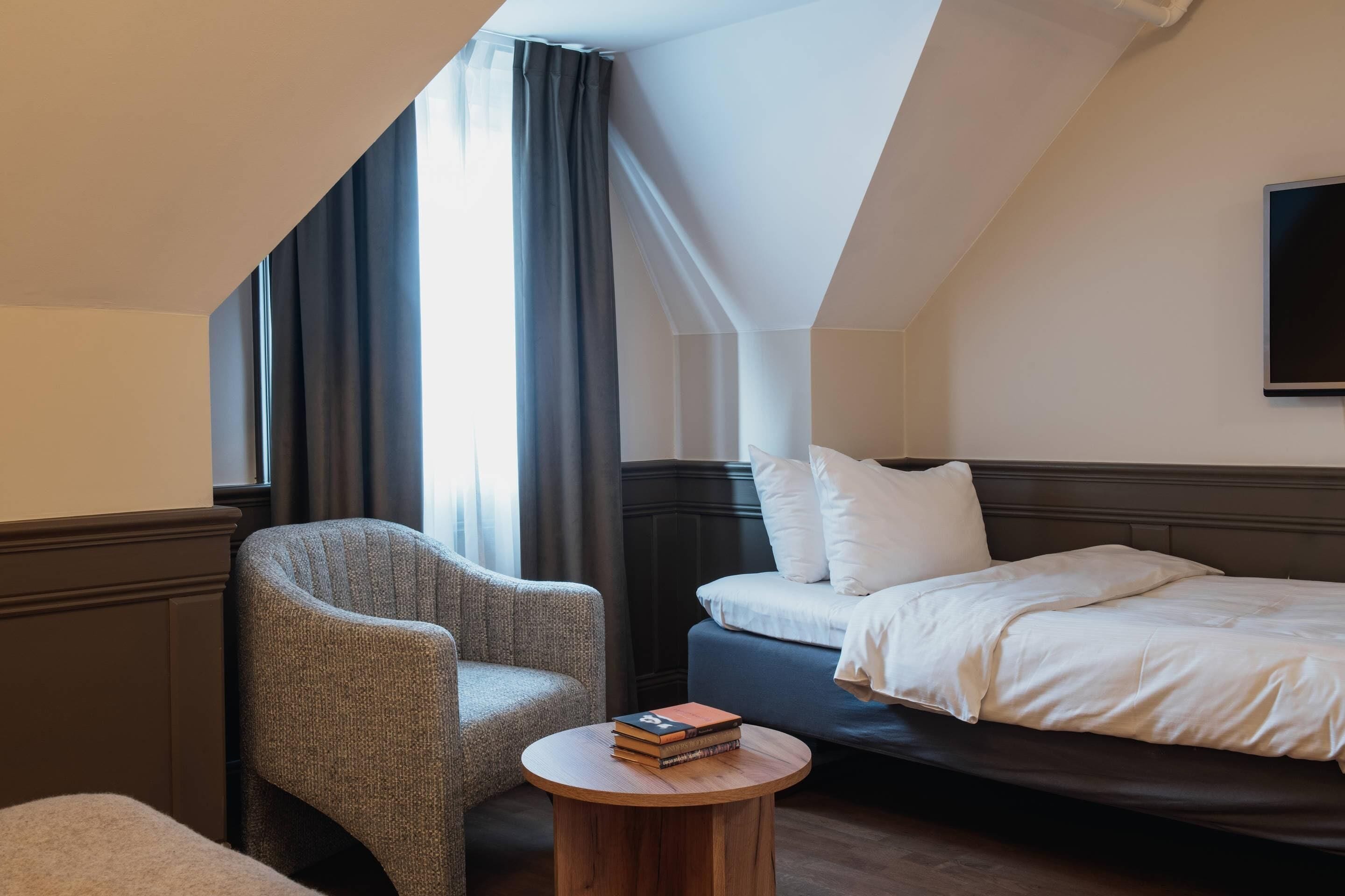 Een hotelkamer met een bed, een stoel, een ronde houten tafel en een televisie aan de muur.