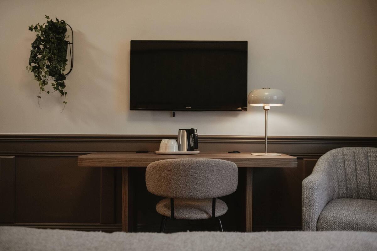 A modern room with a flat-screen TV, a desk with a coffee maker, a lamp, and a chair.