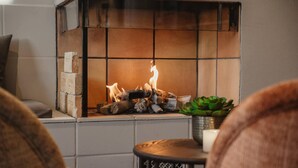 A fireplace with burning logs, a small table with a candle, and a potted plant. - Home Hotel Amanda (Haugesund)