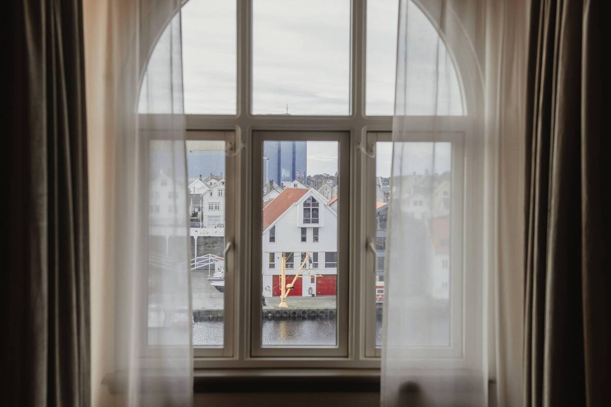 A view through a window with a white frame, looking out to a building with a red roof and a white facade.