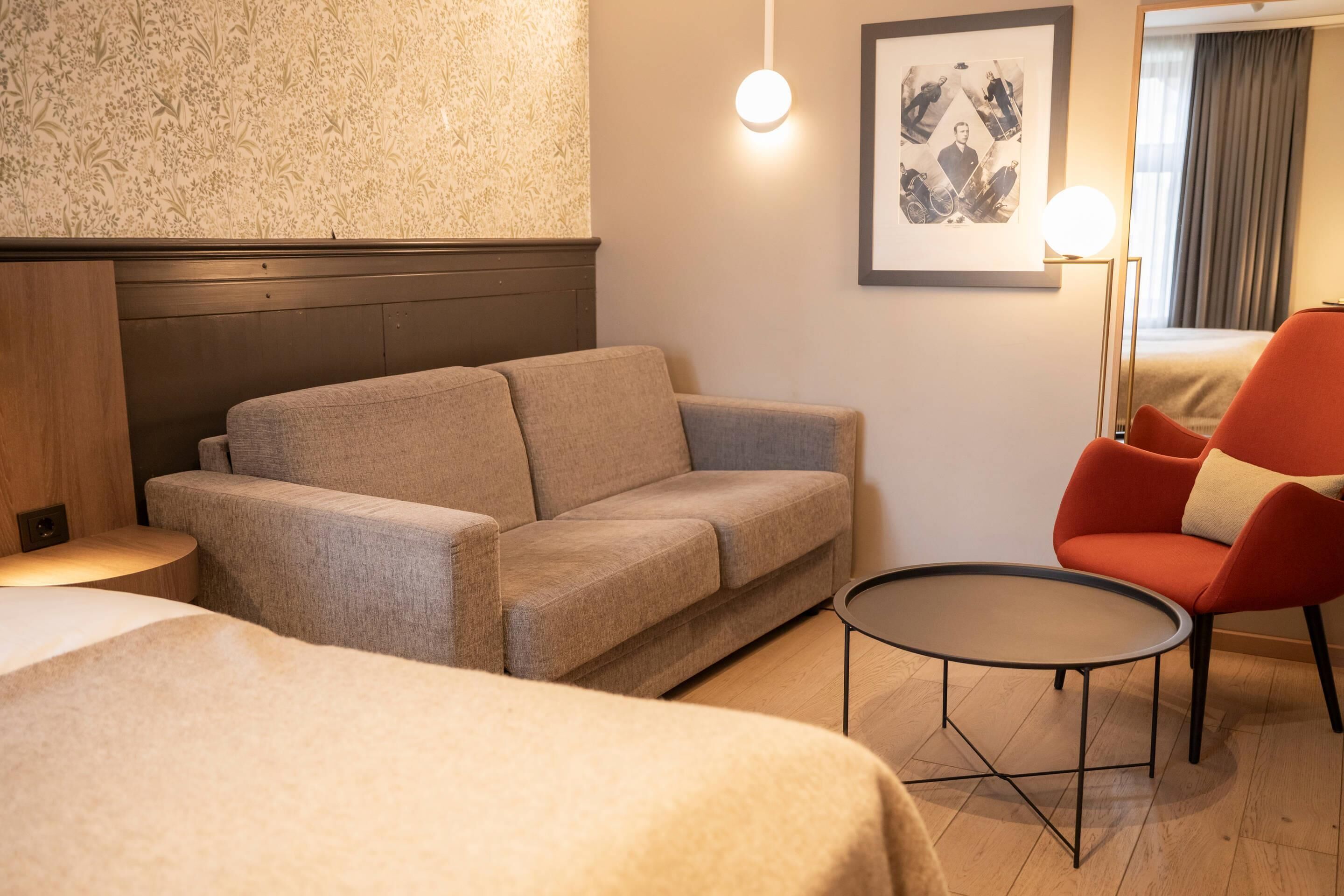Habitación de hotel con sofá, sillón rojo, una mesita redonda y una cama.
