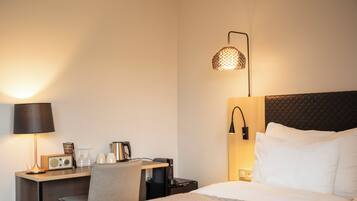 A hotel room with a bed, a desk with a lamp, a radio, and a wall-mounted lamp.
