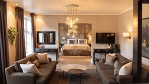 A modern hotel room with a large bed, two sofas, a coffee table, a chandelier, a TV, and a painting on the wall.