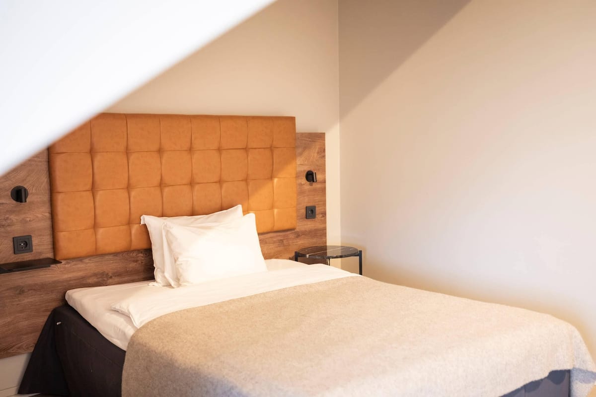 A bedroom with a wooden headboard, a bed with white bedding, and a small bedside table.